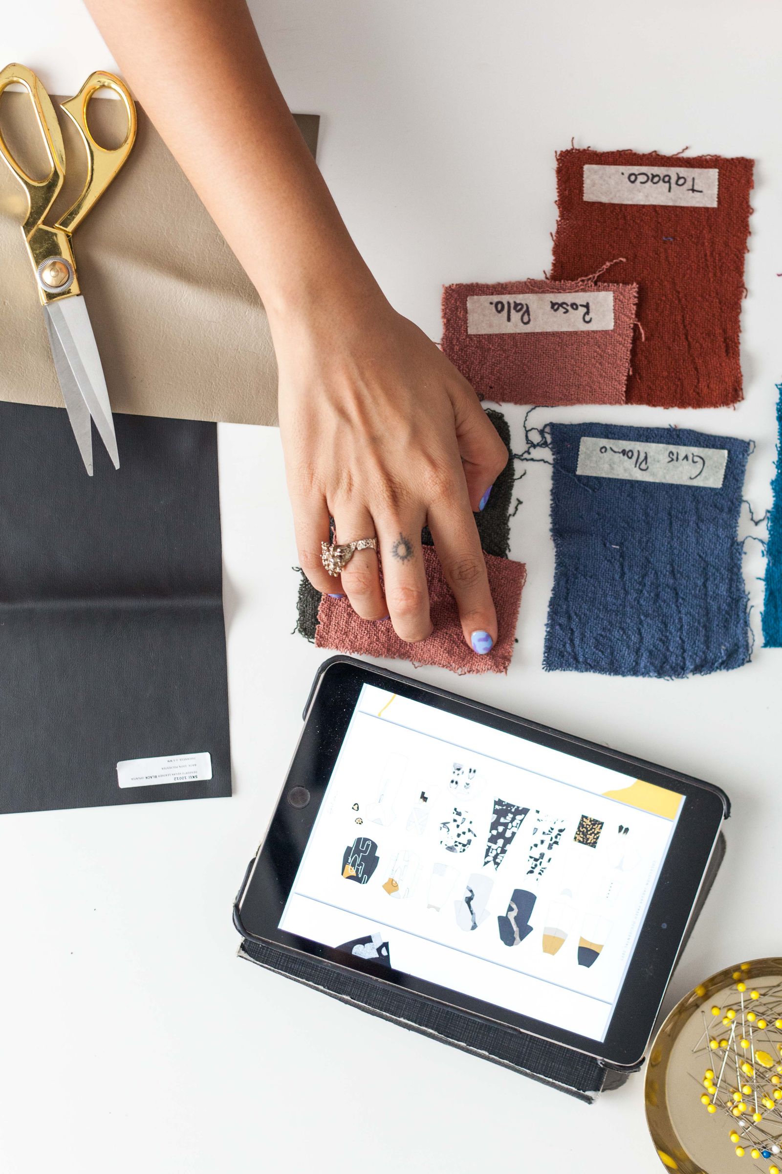 Fabric swatch approval beside fashion sketches, scissors and a digital design board