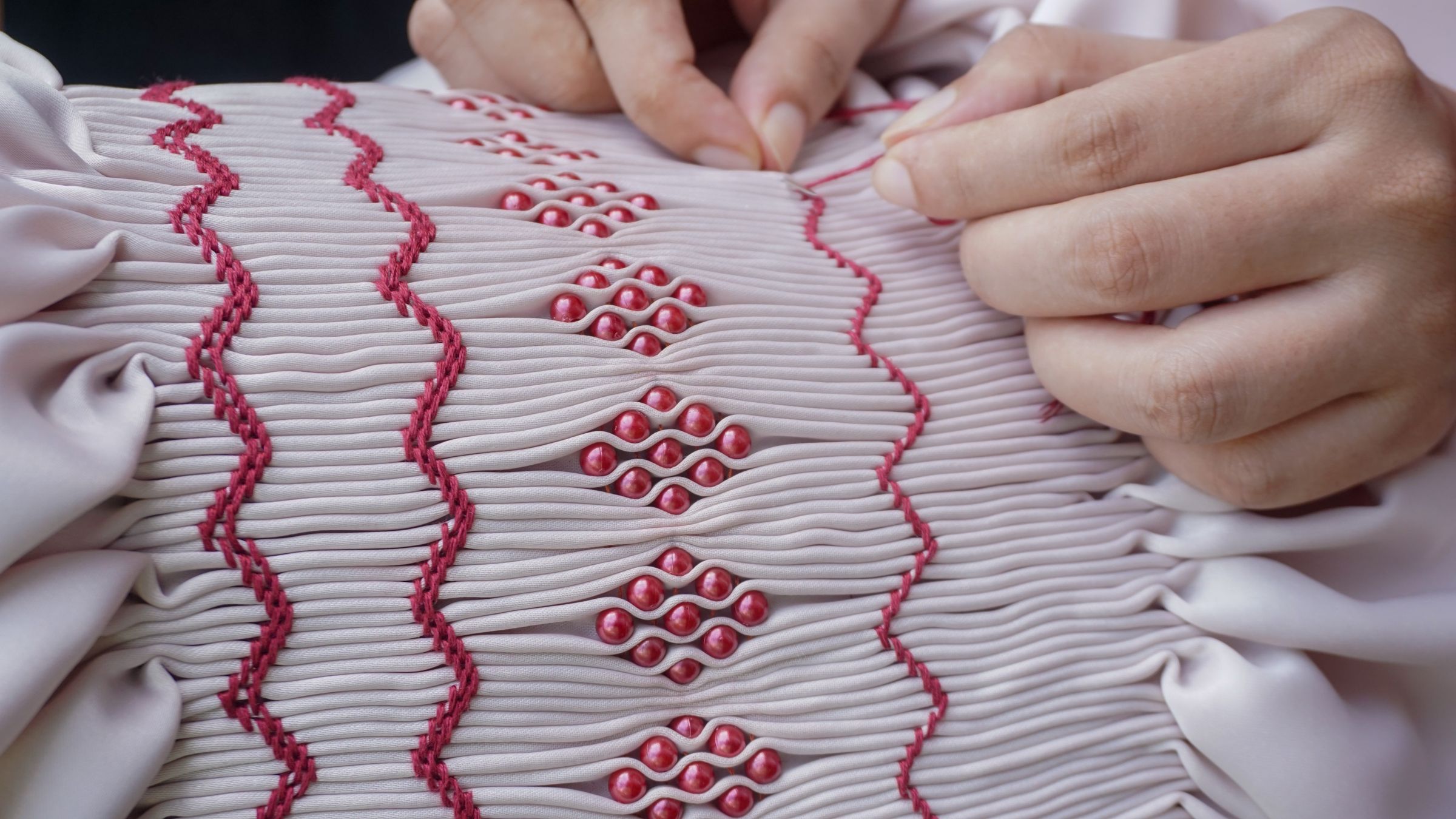 Hands securing decorative beads and embroidery on pleated fabric