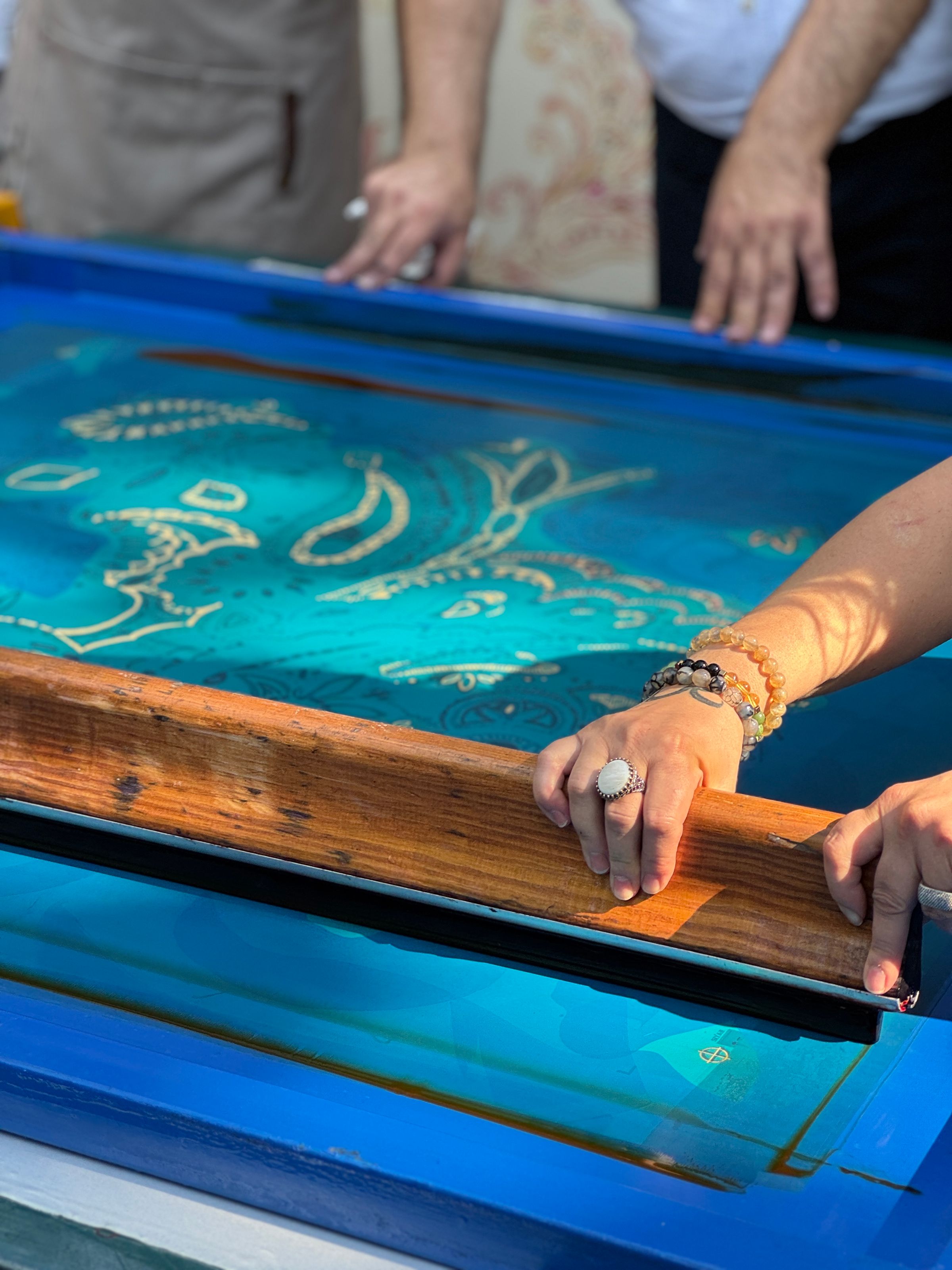 Hands pulling a squeegee across a textile screen-printing frame