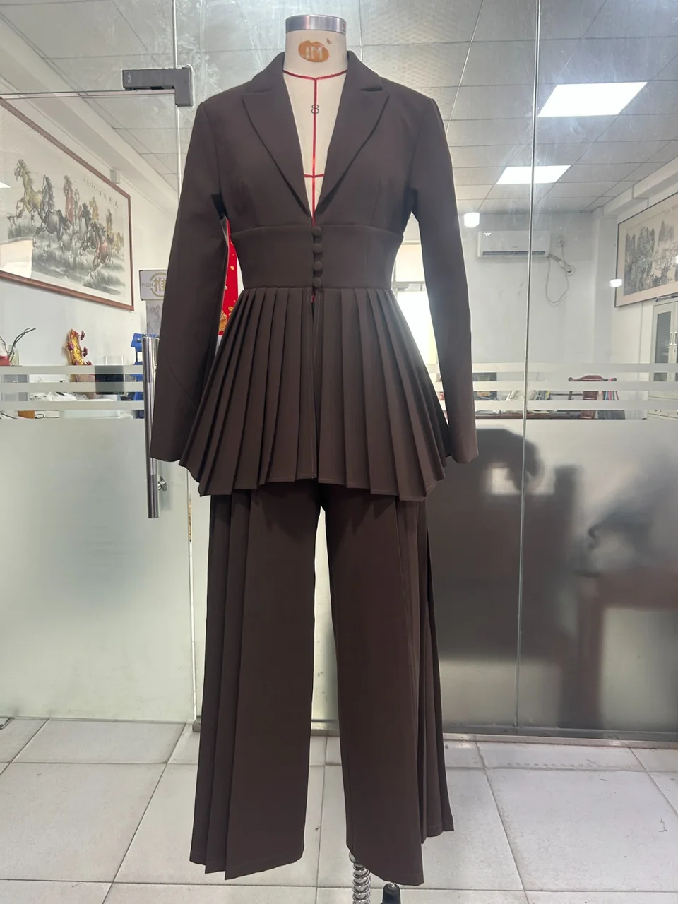 Dark structured peplum jacket and wide-leg trousers, photographed on a mannequin in the workspace
